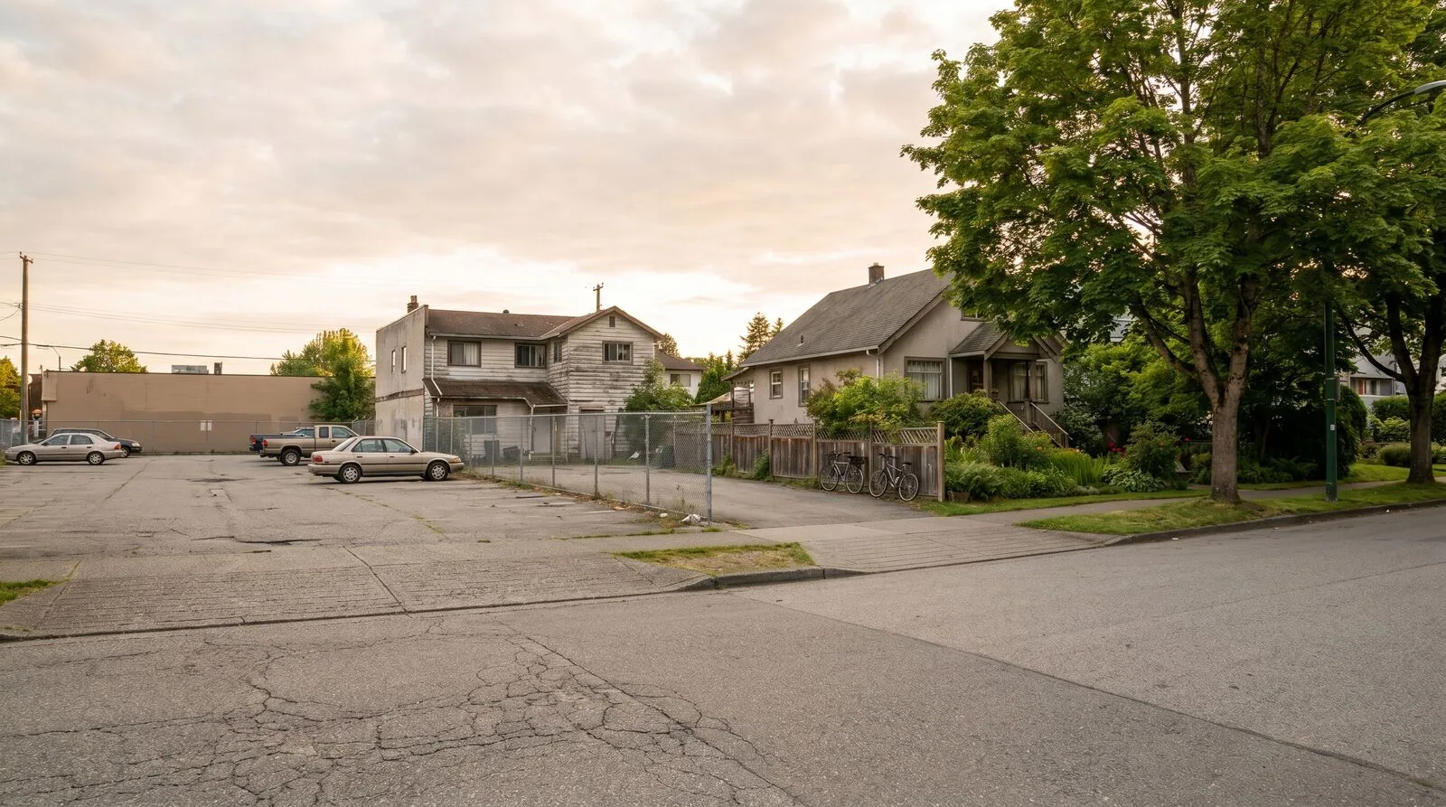 Photograph contrasting a large surface parking lot dominating a residential lot on the left with an older modest single family home with bicycles and street trees on the right of a Vancouver residential street