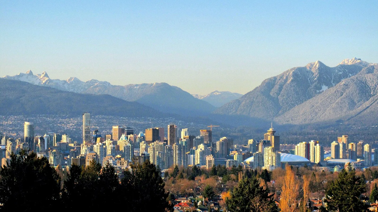 Vancouver skyline with the North Shore mountains behind low-rise residential housing, framing analysis of the May 27 2026 Council vote that reversed the city's all-electric heating rule