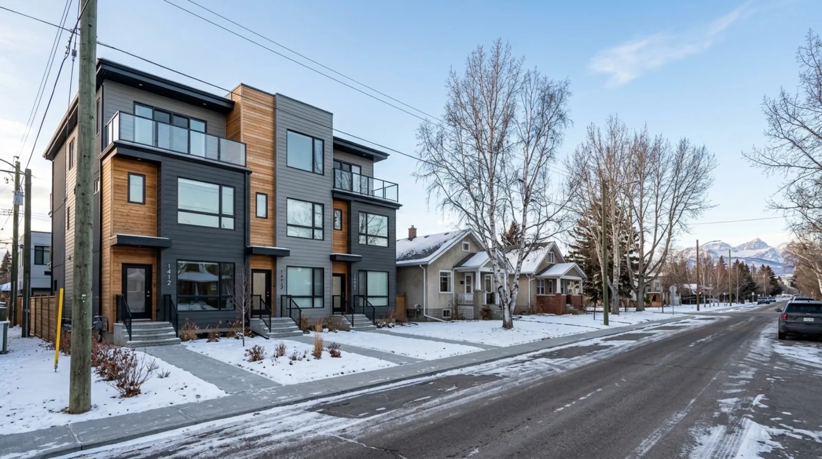 A new rowhouse-style multiplex beside older detached houses on a Calgary residential street, with the Rocky Mountains faint on the winter horizon