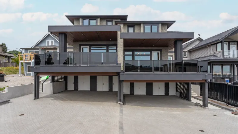 The back of the Majack Developments fourplex on Delestre Avenue in Maillardville, Coquitlam, with parking and storage doors under two second-storey decks and a paved parking court in front